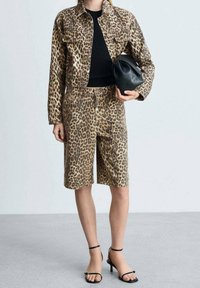 Komplet kurtka i krótkie spodenki w panterkę, wykonany z tkaniny, zestawiony z czarną bluzką i torebką. Strój ma swobodny krój i jest uzupełniony płaskimi sandałami.