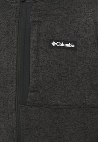 Czarna szara kurtka zapinana na zamek, wykonana z teksturowanego dzianiny, z kieszenią na piersi po lewej stronie oraz białą naszywką z logo Columbia.