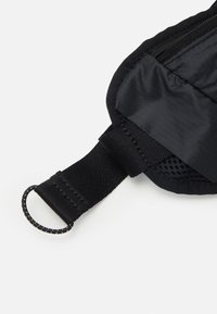 Bolso negro con cremallera que cuenta con un exterior de nailon texturizado, un bolsillo de malla y una correa con bucle para su sujeción. Acabado suave con costuras resistentes.