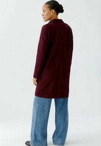 Burgundy wool coat with a collar, long sleeves, and a tailored fit, paired with wide-leg blue denim jeans. Back view shows mid-length design.