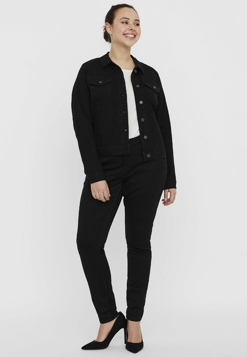 Mustmust denim jakk musta, nupuvääramisega, kahe rinnaeelise taskuga, koos mustade kitsaste pükstega ja mustade terava ninaga kontsakingadega. All on valge topp.