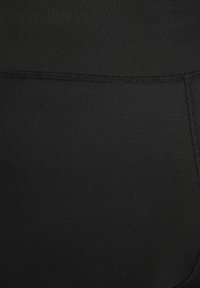 Gros plan d’un tissu noir avec des détails de coutures horizontales et verticales visibles sur un matériau lisse.