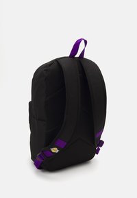 Sac à dos noir avec dos en mesh, bretelles et accents violets, présentant une surface texturée et un détail de logo sur la bretelle inférieure.