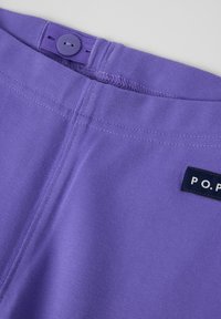 Paars katoenen kledingstuk met knopen sluiting, zichtbare stiksels en een marineblauwe label met de tekst "P.O.P." dicht bij de tailleband.