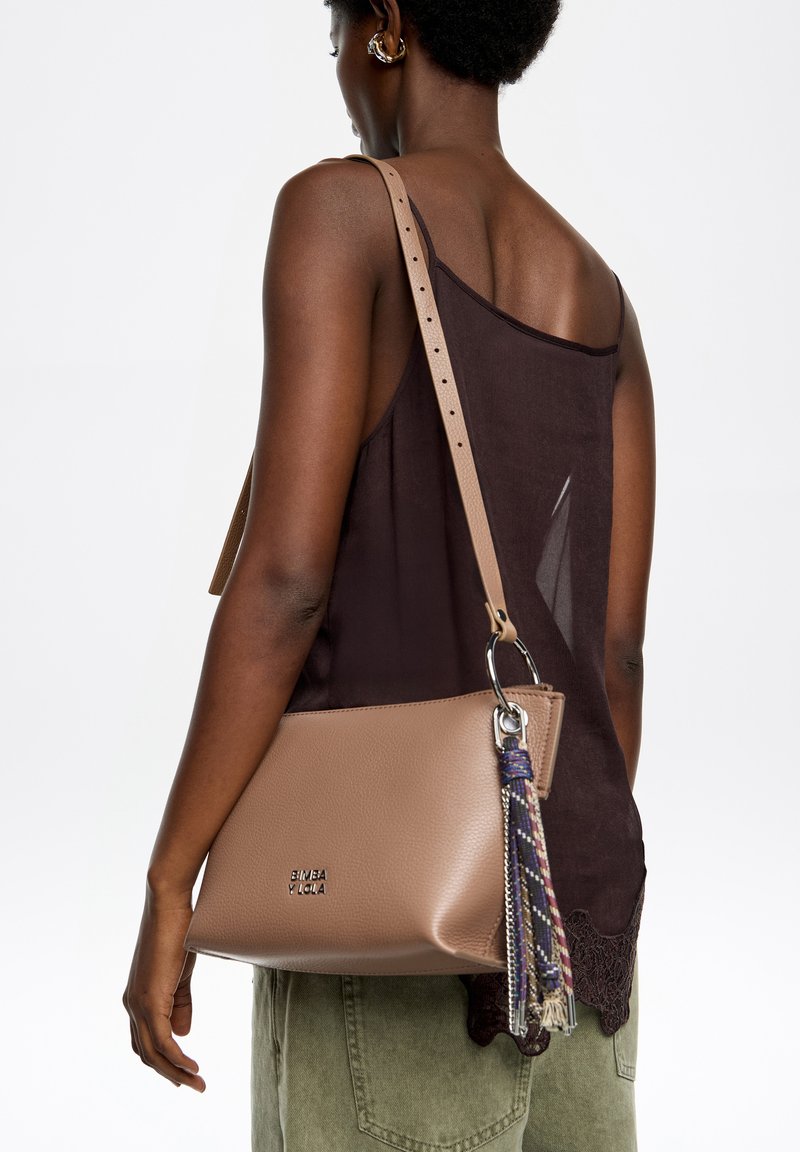 Torba na ramię w kolorze koniakowym z fakturowanym wykończeniem, ozdobiona plecioną frędzlą i srebrnymi elementami. Obecny jest regulowany pasek.