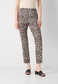 Pantalons ajustés imprimés léopard en beige, marron et noir, avec une jambe droite, des plis avant et une fermeture à bouton. Associés à des mules à talons noires.