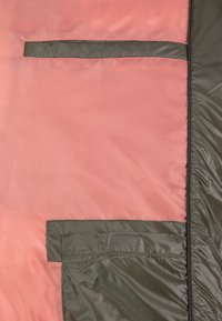 Roze en olijfgroene gewatteerde stof met een gladde textuur, voorzien van een horizontale zak en een geaccentueerde zoomdetail.