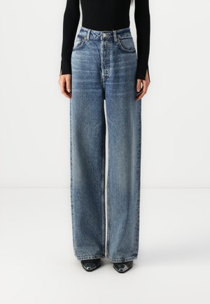 Wide-leg blue denim jeans featuring a high waist, five-pocket design, and subtle texture details, paired with black heeled shoes.