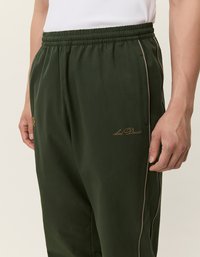 Tmavozelené športové nohavice s textúrovanou látkou, elastickým pásom, bočnými vreckami a zlatou vyšívanou logom.