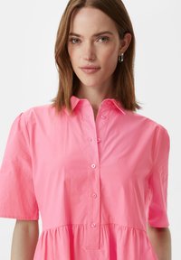 Blusa button-up rosa con maniche corte, caratterizzata da un fit rilassato e orlo arricciato. Tessuto di cotone liscio con bottoni frontali.