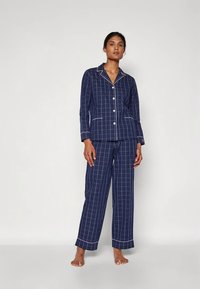 Marinblå pyjamasset med vitt rutmönster, bestående av en knäppt topp med krage och matchande byxor med uppvikta benslut. Mjuk tygstruktur.