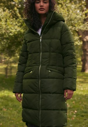 Lång olivgrön puffjacka med hög krage, dragkedja fram och två sidofickor. Har ett quiltat mönster och subtila metalldetaljer.