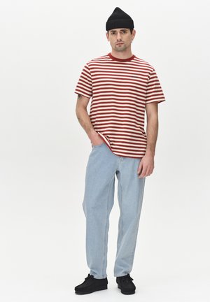 Red and white striped t-shirt, loose fit, paired with light blue jeans. Black knitted beanie and dark shoes complete the look.