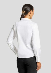Weißes Langarmshirt mit Kragen, geradem Rückennaht und knöpfbaren Manschetten, kombiniert mit schwarzen Hosen. Glatte Textur, taillierte Passform.