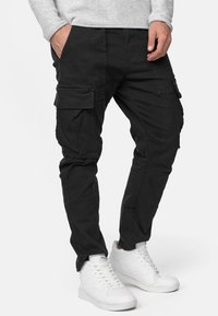 Schwarze Cargo-Hosen mit mehreren Seitentaschen, einem schlanken Schnitt und einem weichen, strukturierten Stoff. Kombiniert mit weißen Sneakers.