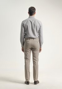 Camisa gris de manga larga, pantalones color beis claros y zapatos marrones. La camisa tiene un cuello y una textura suave; los pantalones tienen bolsillos traseros.