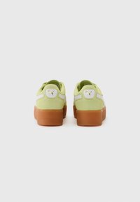 Green suede sneakers with orange rubber soles, white accents, and a gold logo detail on the heel. Rounded shape with padded collar.