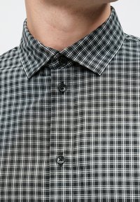 Fekete-fehér kockás ing, hegyes gallérral, elülső gombokkal és hálómintás, texturált anyaggal.