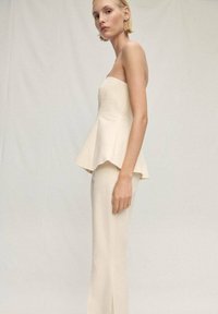 Strapless peplum-topp i krämfärgad tyg med en utsvängd nederdel, kombinerat med figurnära krämfärgade byxor som har en slits framtill. Slät textur överlag.