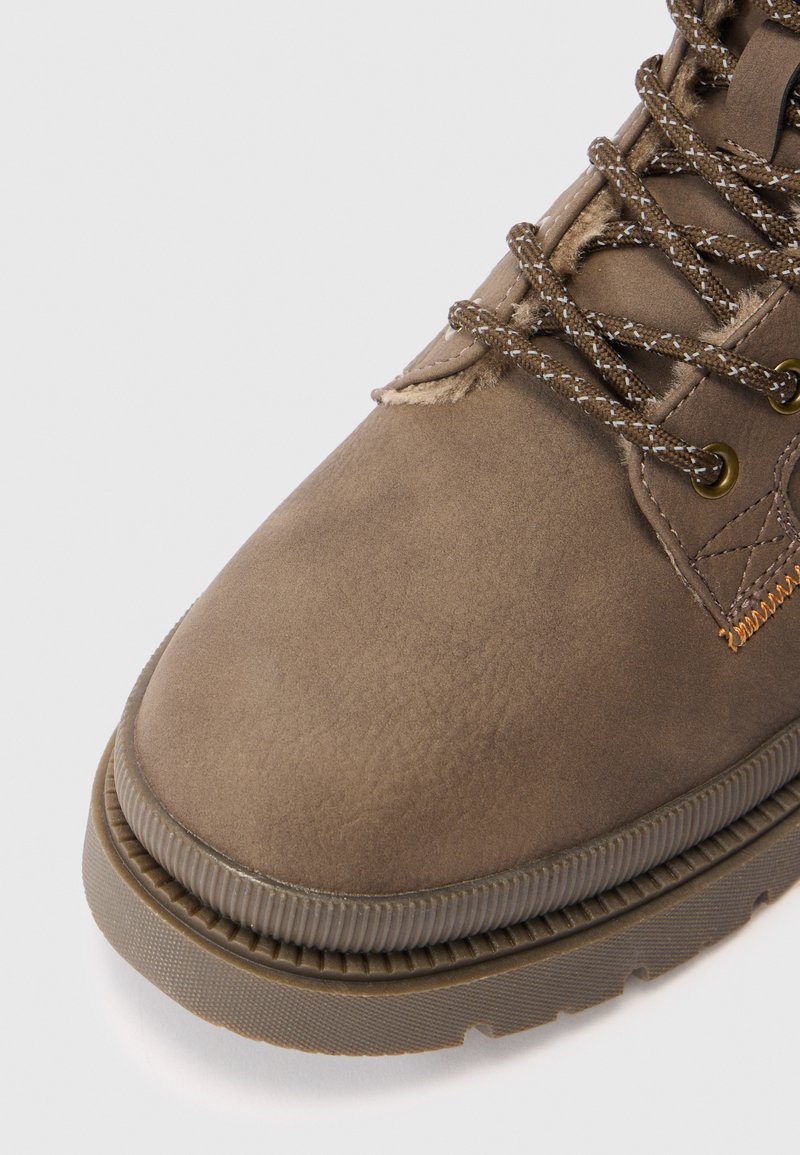 Stivale da trekking in suede marrone, vista frontale, con suola in gomma spessa e lacci marroni a motivo passati attraverso occhielli in ottone.