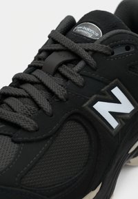 Black running shoe featuring a textured upper, prominent gray mesh accents, thick laces, and a white "N" logo on the side.