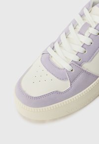 Purple suede and white leather sneaker with flat white laces, perforated toe, and a textured cream rubber sole. Side stitching detail visible.