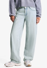 Lichtblauwe wijde spijkerbroek van denim, met een knoopsluiting en voorzakken. Gepaard met witte sneakers. Eenvoudig, casual ontwerp.