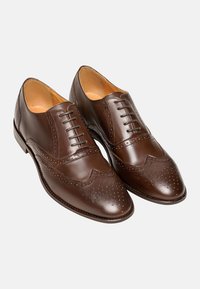 Scarpe eleganti in pelle marrone con design brogue caratterizzato da perforazioni, punta affusolata e una texture liscia. Chiusura con lacci e sei occhielli.