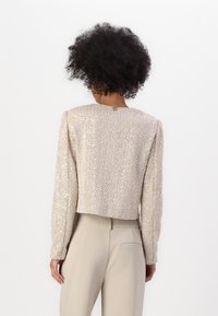 Top corto a maniche corte in tessuto beige chiaro con paillettes, dotato di scollo rotondo e un dettaglio in metallo dorato sul retro.