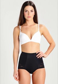 Witte plunge bralette gecombineerd met zwarte high-waisted shorts met uitsparingen. Zachte stof, gladde textuur, minimalistisch ontwerp.
