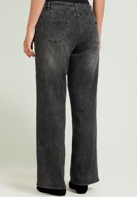 Vaqueros de pierna ancha, de mezclilla negra con un acabado descolorido, cinco bolsillos y trabillas para cinturón. La tela tiene una textura suave y un ligero detalle de desgaste en forma de rayas.