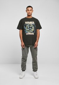 Black graphic t-shirt with a "Nirvana Lithium" design in yellow and blue. Paired with gray cargo pants and white sneakers.