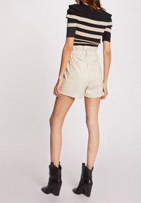 Pull rayé noir et beige avec des manches bouffantes, associé à un short crème taille haute avec des ourlets retroussés et deux poches arrière. Bottes noires à talons.