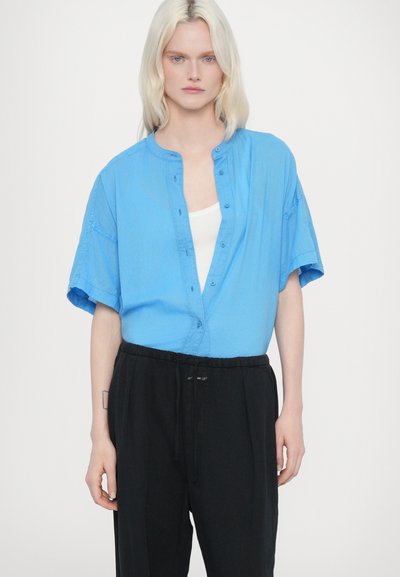 Camicia azzurra a maniche corte con colletto rotondo e vestibilità rilassata, abbinata a pantaloni neri con vita elastica. Design minimalista.