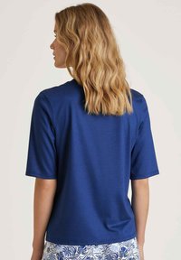 Navy blue short-sleeve top with a crew neckline. Soft, smooth fabric with a relaxed fit, worn with patterned light-colored bottoms.