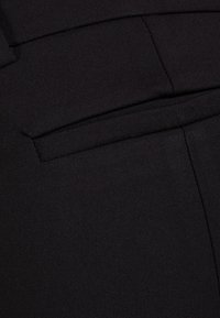 Černá látka s hladkou texturou, která zahrnuje detaily ploché kapsy. Materiál vypadá odolně a je tkaný, s jednotnou barvou po celé ploše.