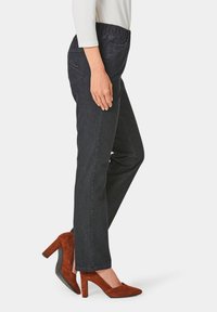 Pantalons en denim bleu foncé avec une taille élastique et une coupe droite. Portés avec des chaussures à talons hauts en suédine marron.