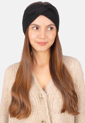 Schwarzes Fleece-Stirnband mit gedrehtem Design, weicher Textur, breitem Band, getragen von einer Person mit langen Haaren, vor einem schlichten Hintergrund.
