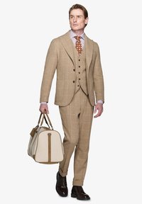 Beige ternet tre-delt jakkesæt med klapkrave, parret med et brunt polka-prikket slips og en lys duffelbag. Brune lædersko.