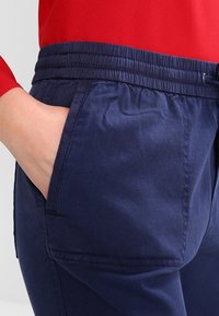 Námořnické modré kalhoty s elastickým pasem a bočními kapsami, vyrobené z hladké látky s jemnou texturou a diagonálními pruhy.