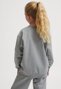 Grå sweatshirt med långa ärmar, ribbat rundhals, och avslappnad passform. Mjuk tyg och sydda fåll detaljer. Bärs med matchande byxor.