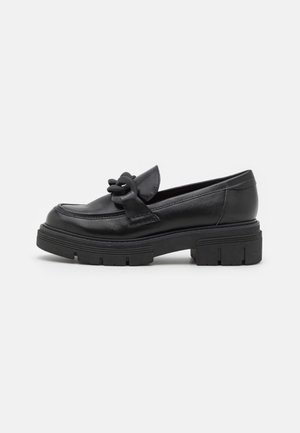 Mocassins en cuir noir avec une semelle en caoutchouc épaisse, ornés d'un nœud décoratif à l'avant et d'un design à bout arrondi.