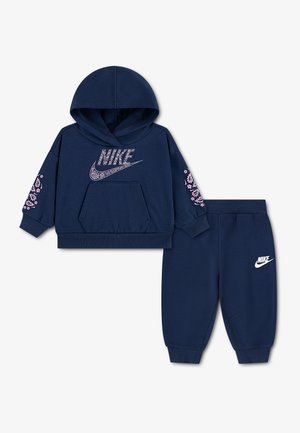 Tmavomodrá Nike mikina s kapucňou pre batoľatá s ružovým paisley logom a akcentmi na rukávoch, v páre s rovnakými tmavomodrými joggermi s bielym Nike logom.