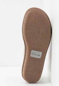 Semelle d'une chaussure marron avec une semelle extérieure en caoutchouc texturé et une étiquette de marque rectangulaire grise près du talon sur fond blanc.