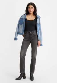 Chaqueta de mezclilla azul claro con bolsillos, top de tirantes negro acanalado, jeans gris de cintura alta y botines negros con tacón.