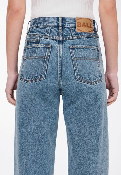 Jeans de mezclilla azul de cintura alta con un ajuste relajado. Presentan un parche de cuero marrón con el logo "BALL", cinco bolsillos y detalles de costura.