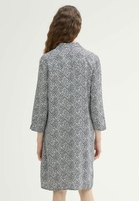 Schwarz-weiß gemustertes Kleid mit Kragen und Dreiviertelärmel, aus leichtem Stoff gefertigt, das hinten über das Knie reicht.
