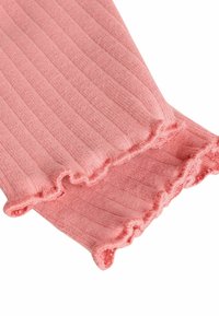 Gros plan d’un tissu tricoté côtelé rose avec des bords froncés sur deux manches ou poignets qui se chevauchent.