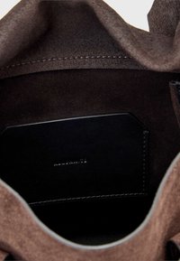 Wnętrze brązowej torebki z zamszu z gładkim czarnym skórzanym kieszonką na karty, z wyraźnymi szwami i miękką fakturą.