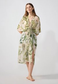 Ανθισμένο κάλυμμα σε στυλ κιμονό από διαφανές ύφασμα, με πράσινα μοτίβα φύλλων, δεμένο στη μέση, V-λαιμόκοψη και πλαϊνές σχισμές για επιπλέον κίνηση.